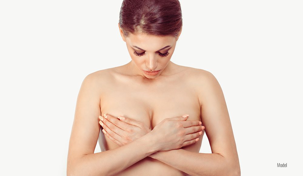 topless woman carefully holds her breasts and looks down at her chest.