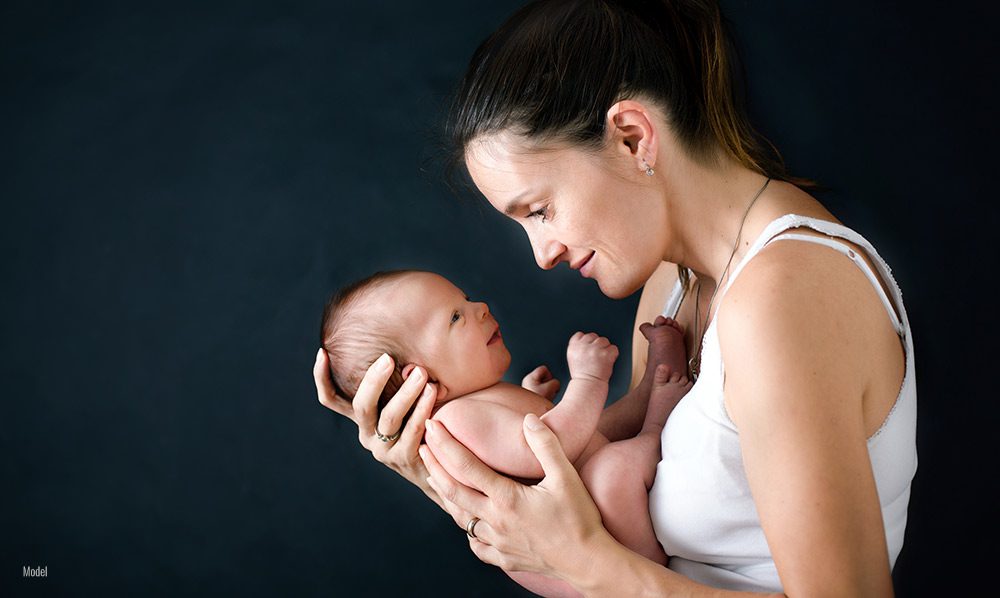 Young mother with dark hair lifts her baby up to her face