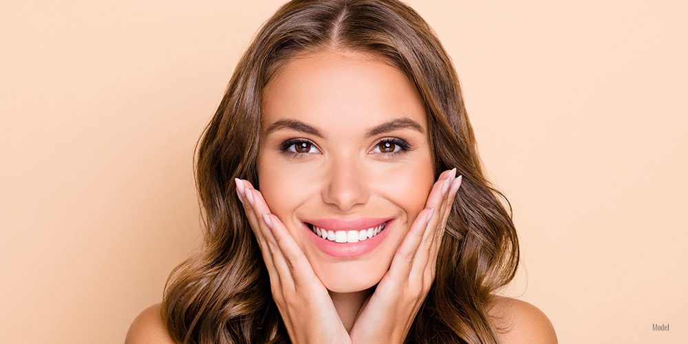 a beautiful woman with long brown hair smiles at the camera against a tan background