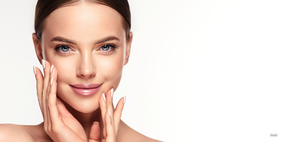 a woman with natural makeup and smooth skin smiles into the camera against a white background