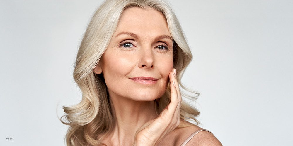 portrait of a mature blonde woman smiling at the camera with flawless skin and natural makeup.